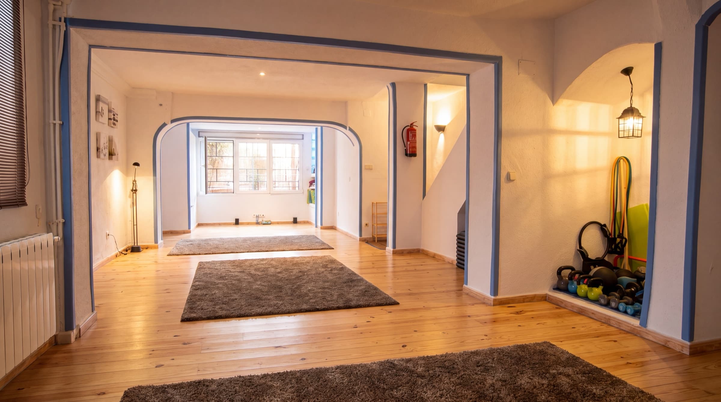 Sala de práctica de Yoga Bambú: suelo de madera clara, paredes blancas con arcos ribeteados en azul y luz natural desde el ventanal.